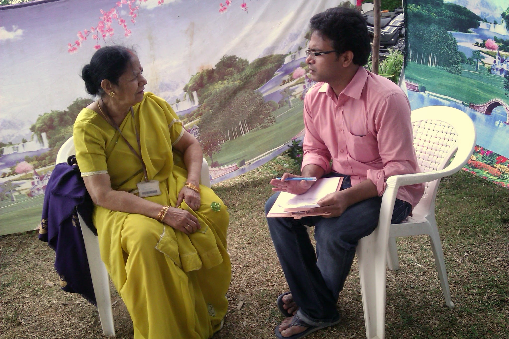 Dr. Suresh sitting on a plastic chair on the grass with a clipboard listening one-on-one with humility to a mother and grandmother